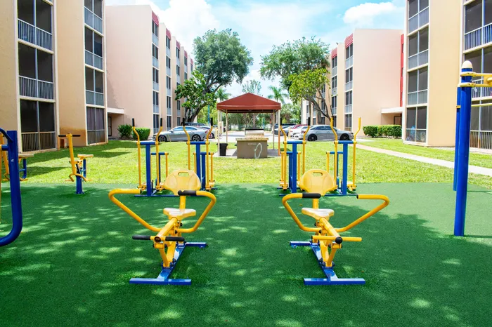 Inviting outdoor fitness area surrounded by modern apartment buildings with lush greenery and vibrant exercise equipment.