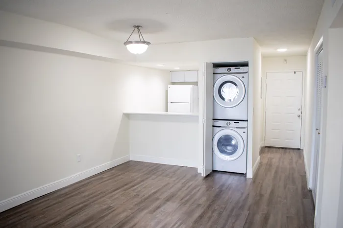 Modern apartment interior with sleek wood flooring, stacked washer and dryer, and a stylish kitchen area.