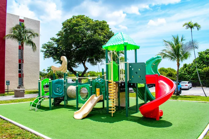 Vibrant playground with green and red slides, perfect for family-friendly living in a sunny apartment community.