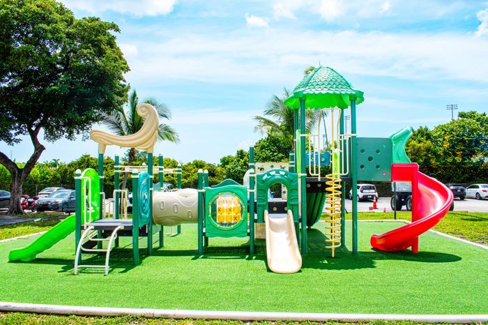 Vibrant playground with colorful slides and climbing structures set against a backdrop of lush greenery and blue skies.