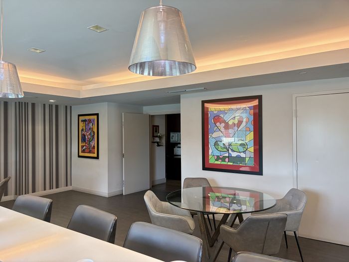 Bright dining area with modern glass table, chic gray chairs, and vibrant abstract artwork on the walls, enhanced by stylish pendant lighting.
