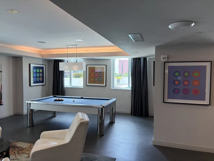 Luxurious lounge area featuring a sleek pool table, modern artwork, and large windows offering ample natural light.