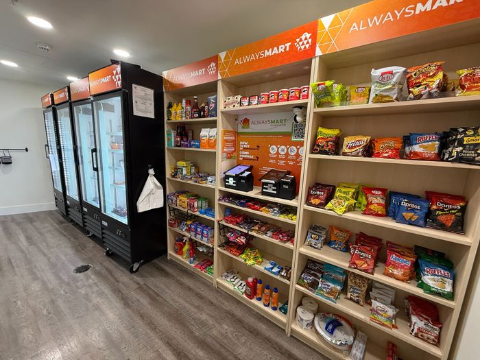 Modern self-service snack corner with well-organized shelves stocked with a variety of chips, snacks, and beverages in a bright convenience area.