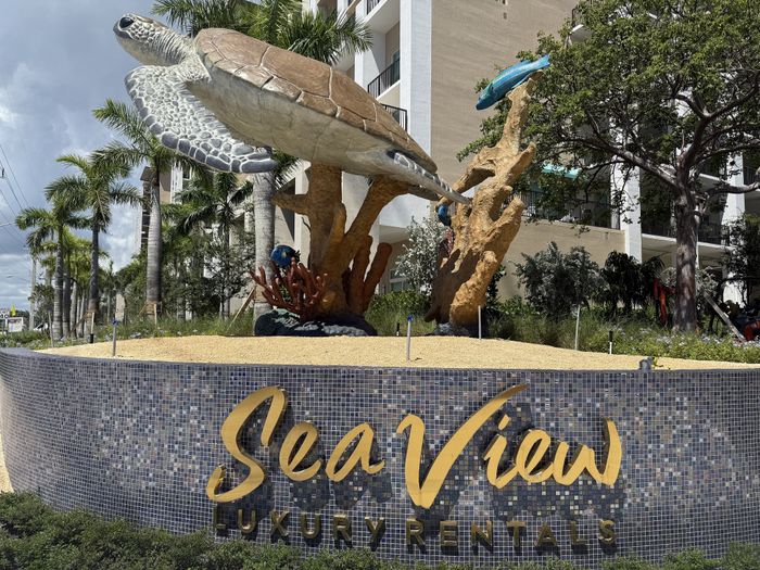 Inviting entrance of Sea View Luxury Rentals with stunning turtle sculpture, lush greenery, and modern architecture.