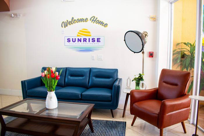 Inviting living area at Sunrise Village Apartments featuring a navy blue sofa, a cozy brown leather armchair, and vibrant tulips on a chic coffee table.