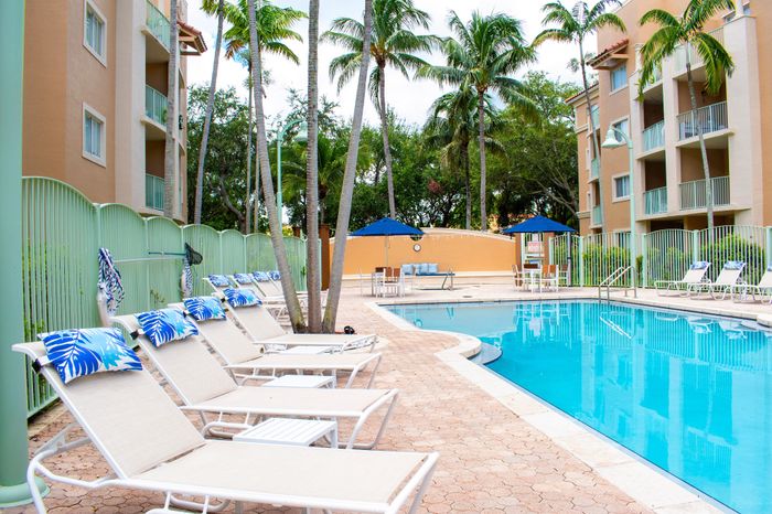 Luxurious poolside oasis with stylish loungers and lush palm trees, surrounded by modern apartments and vibrant greenery.