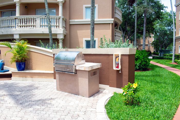 Elegant outdoor area with a modern stainless-steel grill, lush greenery, and stylish architecture offering a serene lifestyle.