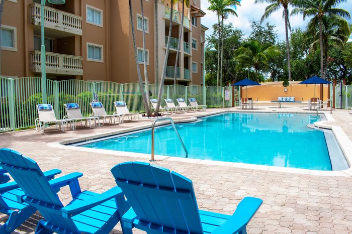 Inviting outdoor pool area with vibrant blue chairs, surrounded by lush palm trees and a stylish apartment building.