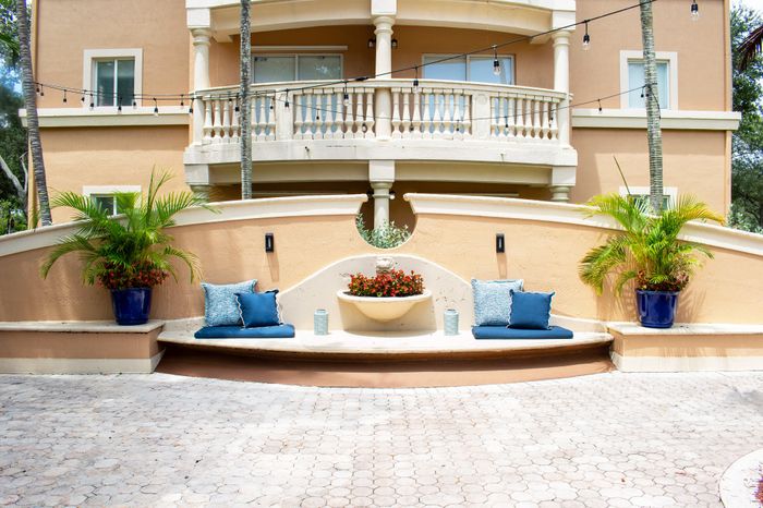 Charming outdoor seating area with plush blue cushions, tropical plants, and warm orange facade, ideal for relaxation.