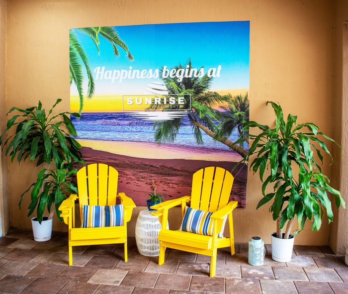 Bright and inviting patio area at Sunrise Village with yellow chairs, tropical decor, and a vibrant beachfront mural.