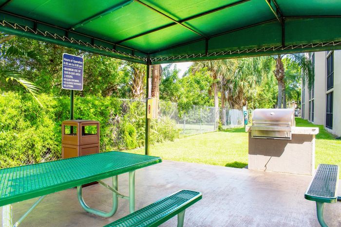 Charming outdoor BBQ area with lush greenery, picnic table, and covered seating, perfect for gatherings and relaxation.
