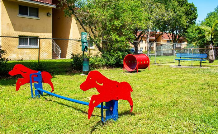 Charming apartment complex dog park featuring vibrant red agility equipment on lush green grass, perfect for pet owners.