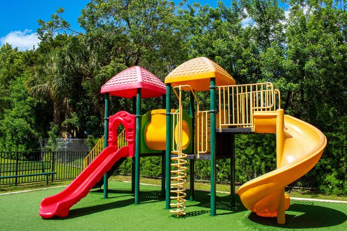 Bright and colorful playground with slides and climbable structures surrounded by lush greenery, perfect for children.