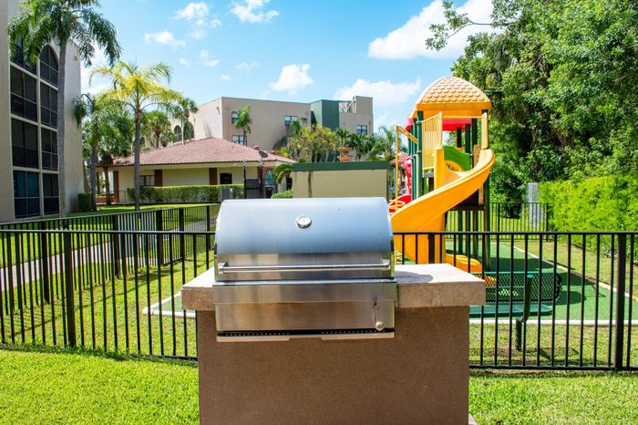 Inviting community outdoor space featuring a stainless steel barbecue grill and vibrant playground set amidst lush greenery.