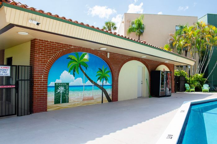 Inviting poolside area featuring a vibrant beach mural, surrounded by lush greenery and comfortable seating.