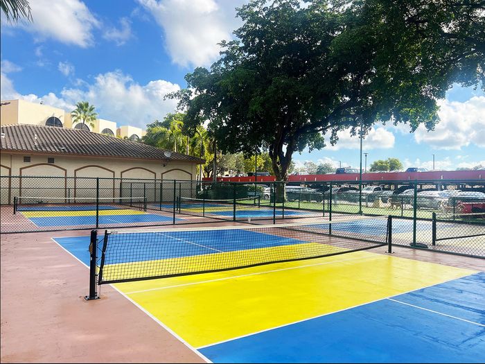 Vibrant outdoor pickleball courts with colorful blue and yellow surfaces surrounded by lush greenery and ample amenities.