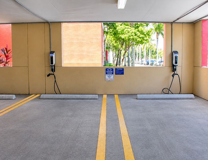 Modern parking area featuring electric vehicle charging stations set against a vibrant backdrop of lush greenery and bright architecture.