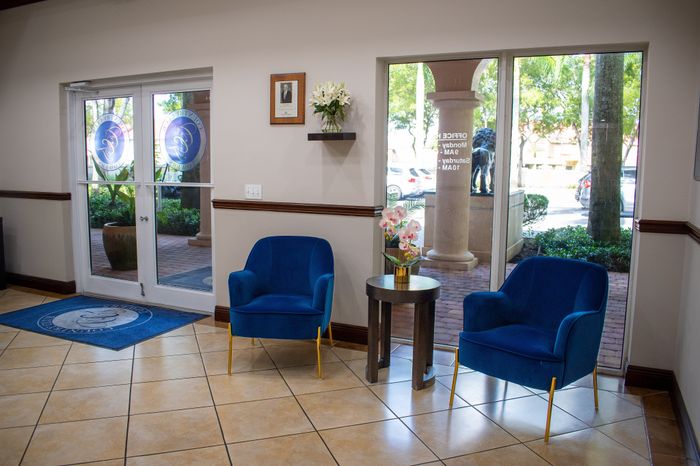 Inviting lobby area with elegant blue chairs, tiled flooring, and large glass doors opening to lush greenery.