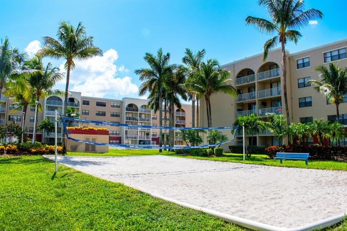 Vibrant apartment complex with lush greenery, palm trees, and a sand volleyball court, ideal for outdoor activities and relaxation.