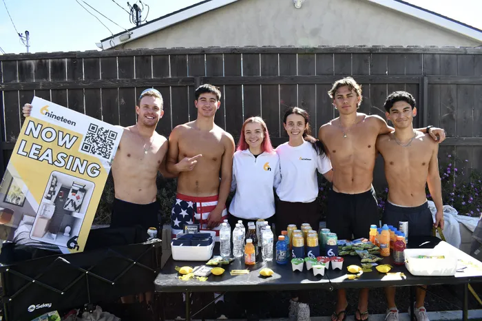 Two leasing team members stand smiling between four shirtless students posing in front of a table of refreshments and a