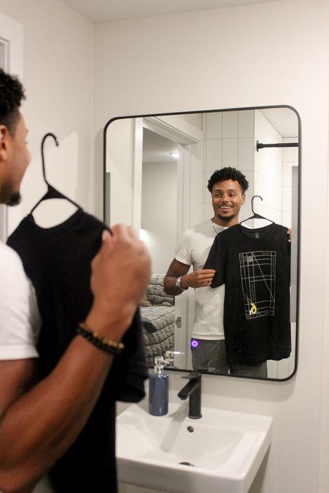 A man examines a shirt while looking at his reflection in a mirror.