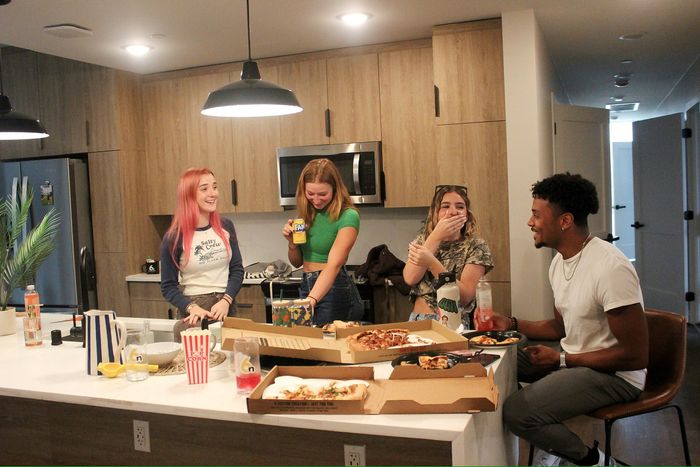 4 friends laughing, eating pizza in the kitchen.