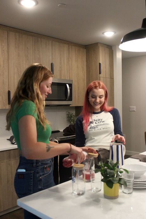 Woman in a green shirt pouring a drink for red haired friend.