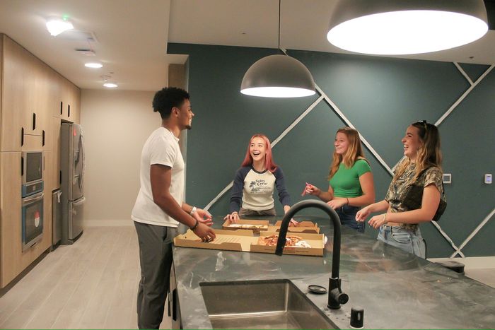 4 friends gathered around the kitchen island sharing pizza and laughing.