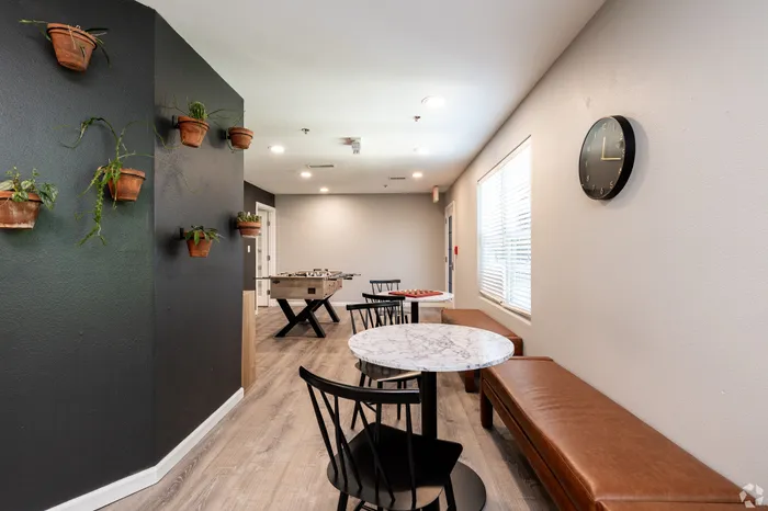 Modern apartment community game lounge with marble-top tables, bench seating, wall-mounted plants, and a foosball table, offering a stylish indoor space for residents to relax and socialize.