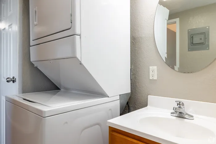 Apartment bathroom featuring an in-unit stacked washer and dryer beside a vanity sink with mirror, offering convenient laundry access within a functional, space-saving layout.