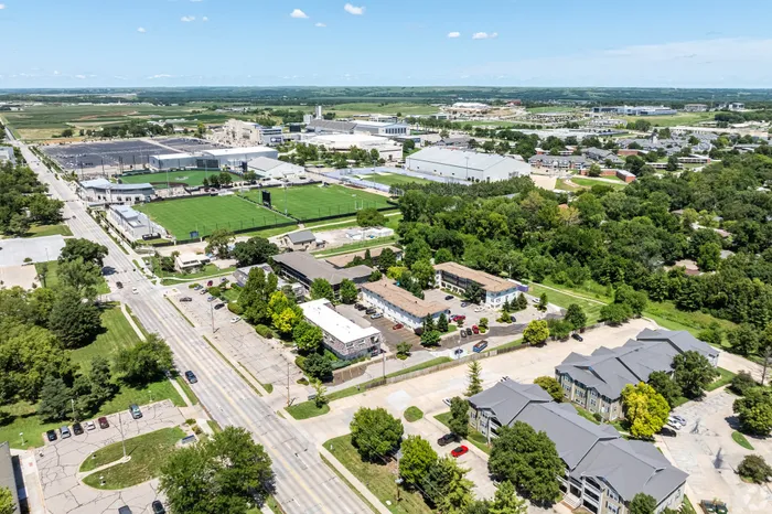 Aerial view of a residential apartment community near athletic fields, campus buildings, and tree-lined streets, highlighting a convenient location with nearby green space and local amenities.
