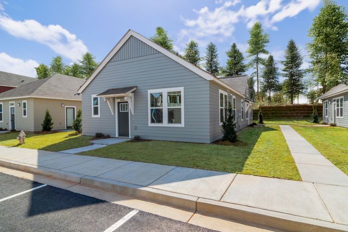 Charming and modern single-story home with beautiful gray siding, large windows, and a welcoming front door, nestled in a peaceful neighborhood with lush greenery and clear blue skies.