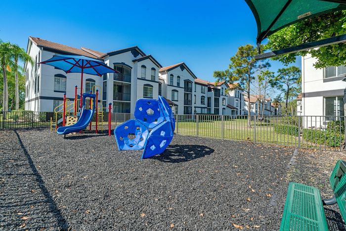 Charming apartment complex with modern playground, featuring lush landscaping and bright blue skies.