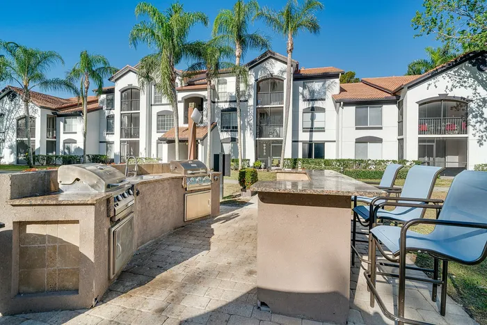 Luxurious outdoor barbecue area with sleek grills, set against elegant white apartment buildings and lush palm trees.