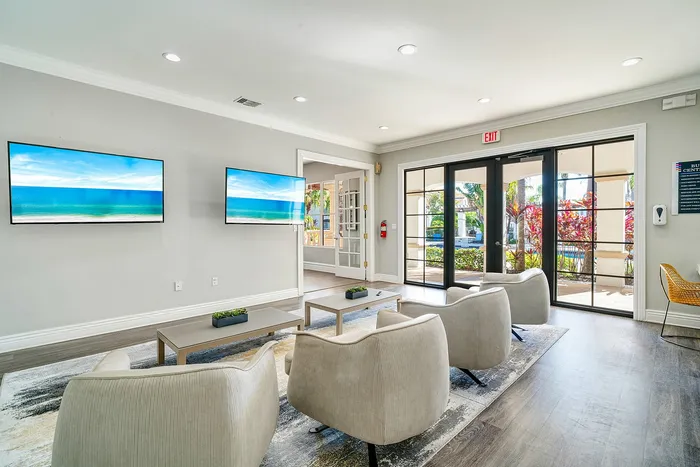 Bright and inviting modern living area featuring cozy seating, large windows with garden views, and dual wall-mounted screens.