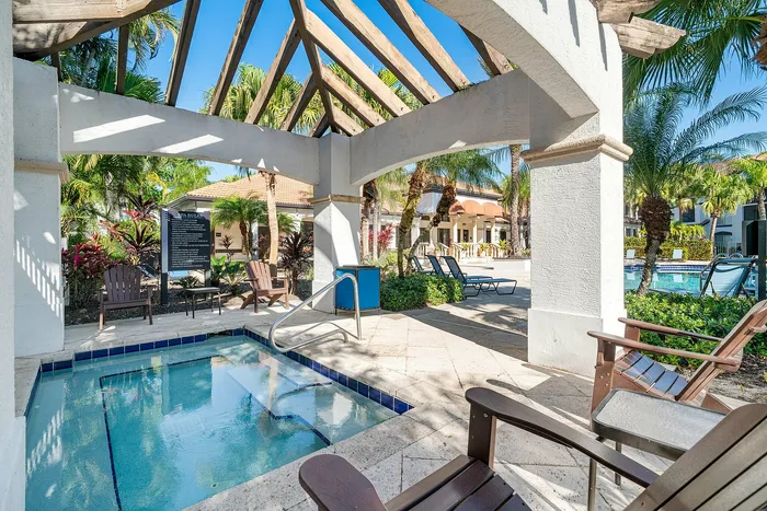 Inviting outdoor lounge area with a serene spa at an elegant apartment complex, surrounded by lush tropical landscaping and stylish lounging chairs.