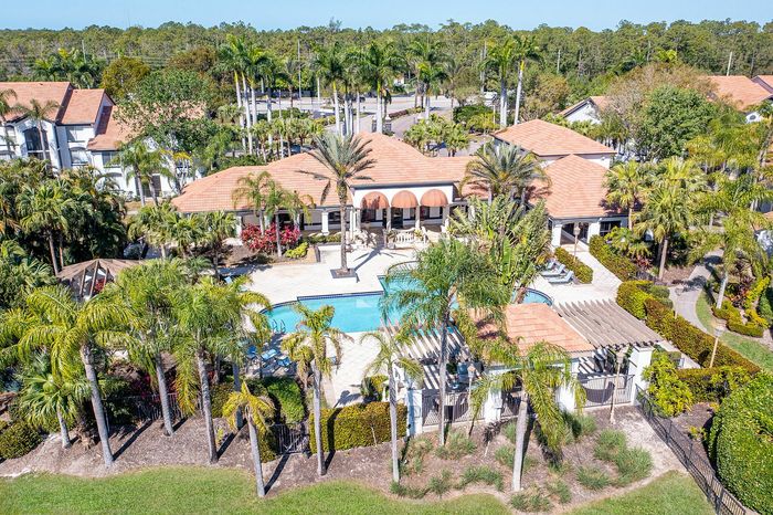 Luxurious aerial view of a resort-style apartment complex with a sparkling pool, lush gardens, and elegant terracotta rooftops surrounded by palm trees.