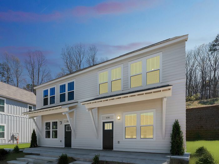 Charming modern duplex exterior with large windows, surrounded by lush greenery under an expansive sky.