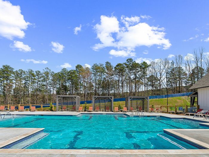 Inviting outdoor pool with sun loungers and scenic wooded backdrop under a bright blue sky.