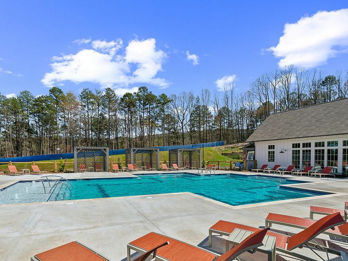 Inviting outdoor swimming pool with stylish sun loungers under a clear blue sky, surrounded by serene greenery and modern architecture.