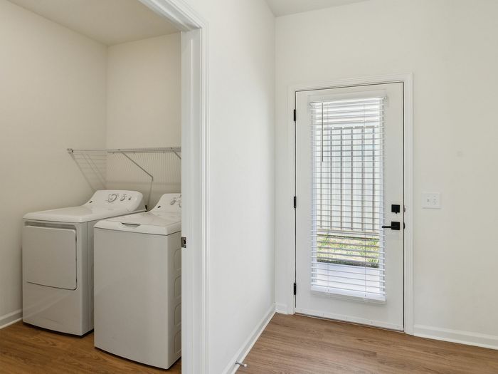 Modern laundry room with sleek washer and dryer, featuring wooden floors and a door with elegant blinds.