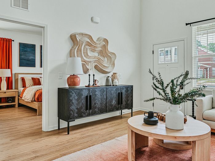 Inviting living room with stylish decor, featuring a wooden coffee table, elegant sideboard with decorative vases, and a glimpse into a cozy bedroom with vibrant orange accents.