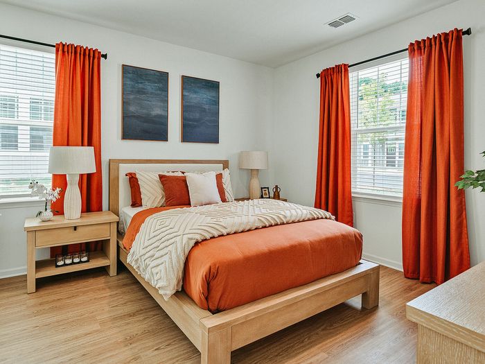 Inviting bedroom with bright orange accents, modern wooden furniture, and natural light streaming through large windows.