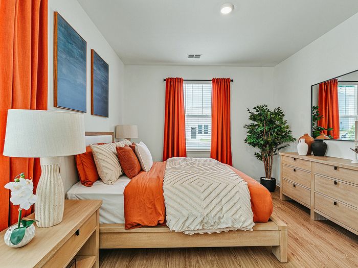 Inviting bedroom with vibrant orange accents, featuring a cozy bed, stylish wooden furniture, and natural lighting.