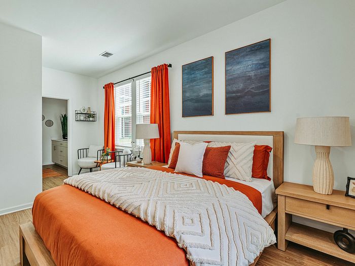 Inviting bedroom with vibrant orange accents, cozy bedding, and ample natural light, complemented by modern decor and a stylish ensuite bathroom.