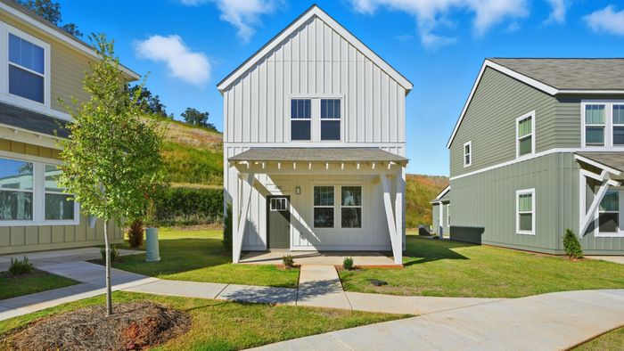 Charming modern home with classic white facade, surrounded by lush greenery and a clear blue sky backdrop, offering serene living.