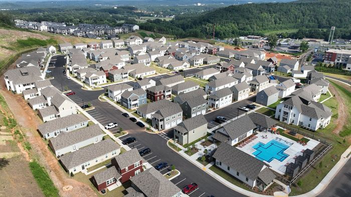 Charming aerial view of a vibrant residential community featuring modern houses, scenic greenery, and a refreshing swimming pool.