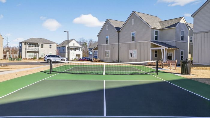 Charming suburban community with modern homes featuring a tennis court surrounded by fresh landscaping under a bright blue sky.