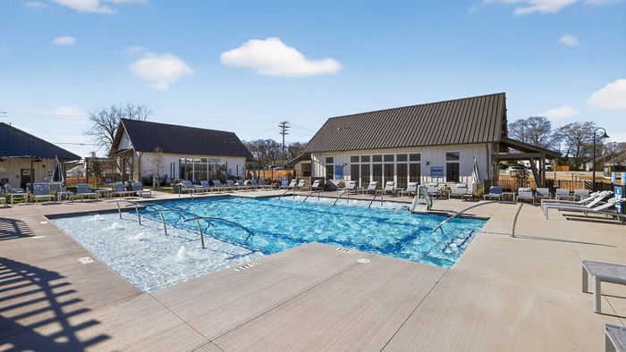 Inviting outdoor pool area with modern sun loungers and charming clubhouse under a bright blue sky.