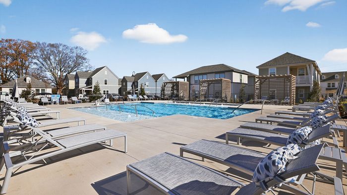 Inviting outdoor pool area with elegant lounge chairs and modern cabanas set against a backdrop of charming houses under a clear blue sky.